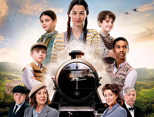 A movie poster for "The Railway Children Return" featuring a group of children and adults arranged around the front of a steam train marked 5596, with rolling hills and a stone viaduct behind them. Set against a warm sky with the tagline "A New Adventure Begins".